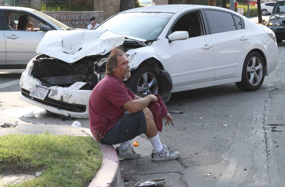 Don Hackman, 58, sits on the curb of Nordhoff Street and Darby Avenue after the white Nissan Altima (behind) crashed into his black Chevrolet truck on Wednesday. Photo Credit: Mariela Molina