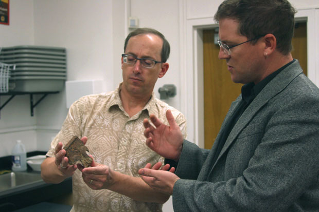 Dr. James Smead, director of the Anthropological Research Institute and archeology professor, reveals to Dr. Matthew Des Lauriers, fellow anthropology colleague, a fragment of equipment from the 1928 St. Francis Dam Disaster. Photo Credit: Andrea Alexanian