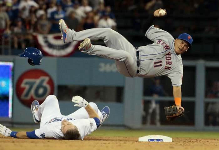 A+Dodger+player+falls+onto+the+ground+as+his+opponent+%28New+York+11%29+jumps+over+him+to+throw+the+ball.