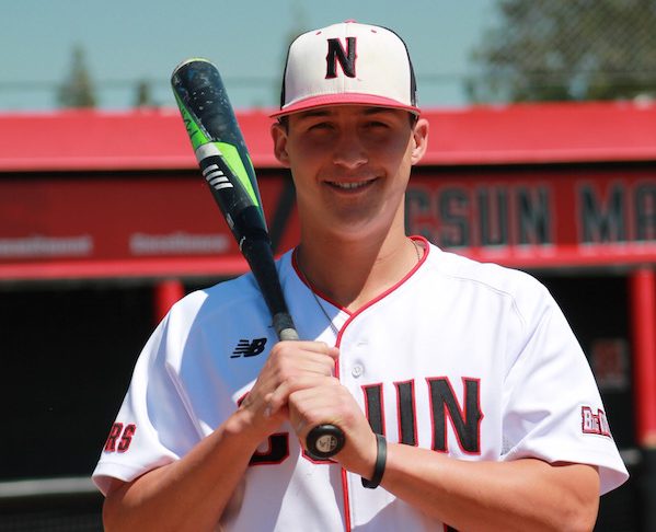 CSUN baseball athlete carries baseball bat while smiling
