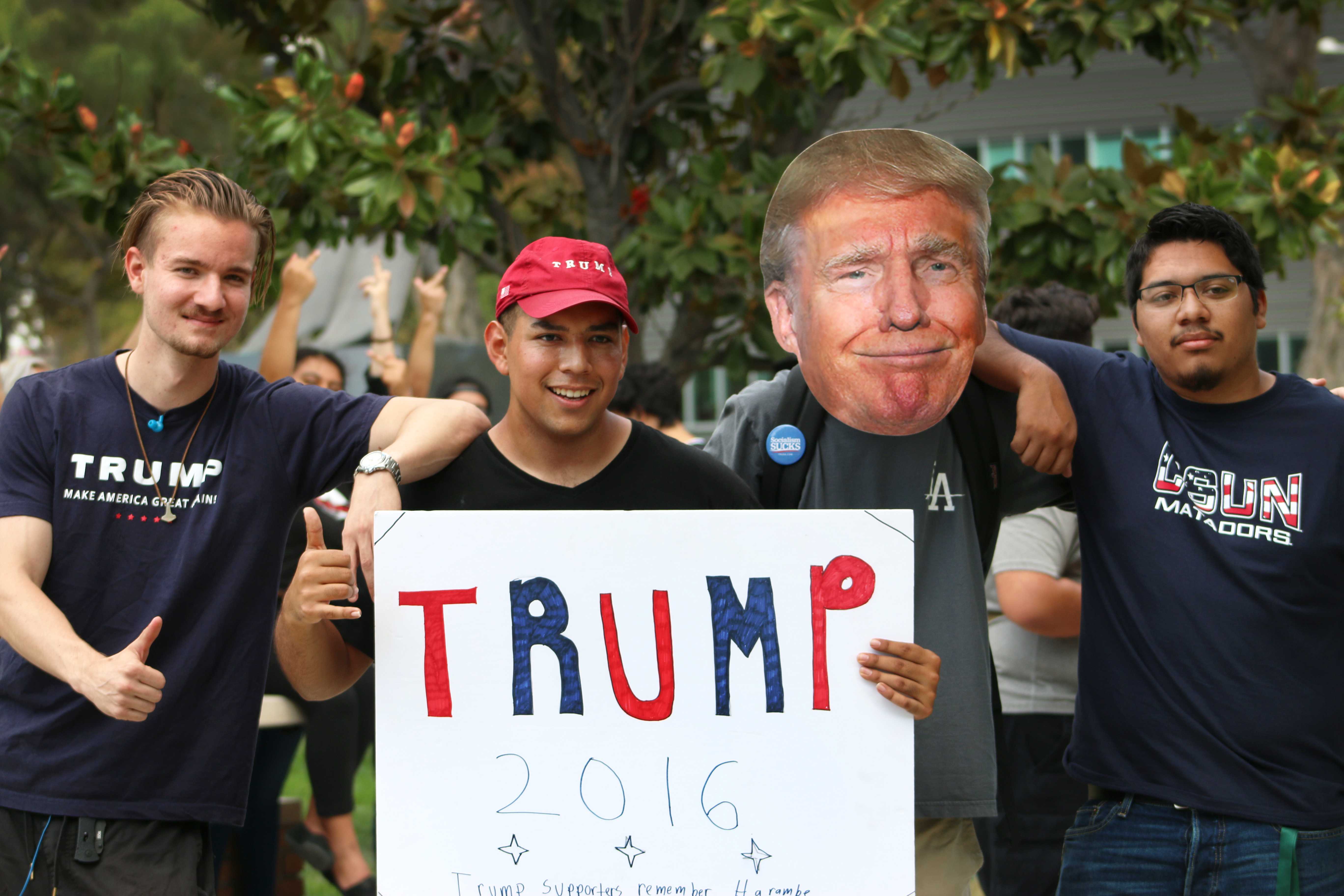 Trump+supporters+hold+up+trump+2016+poster+while+people+in+the+background+flip+them+off