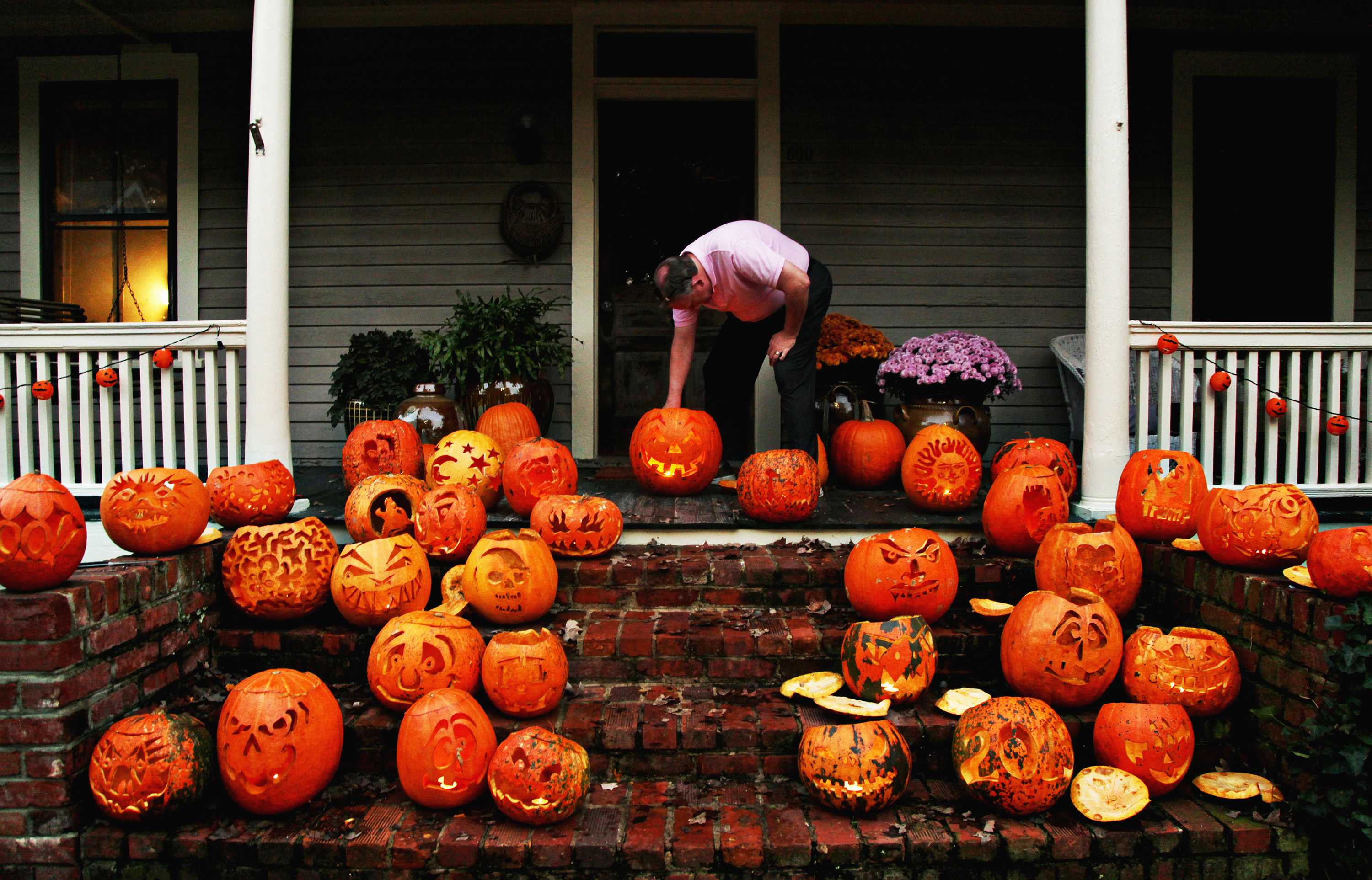 Man shown in front of house setting up approximately 20 different jack-o-lanterns