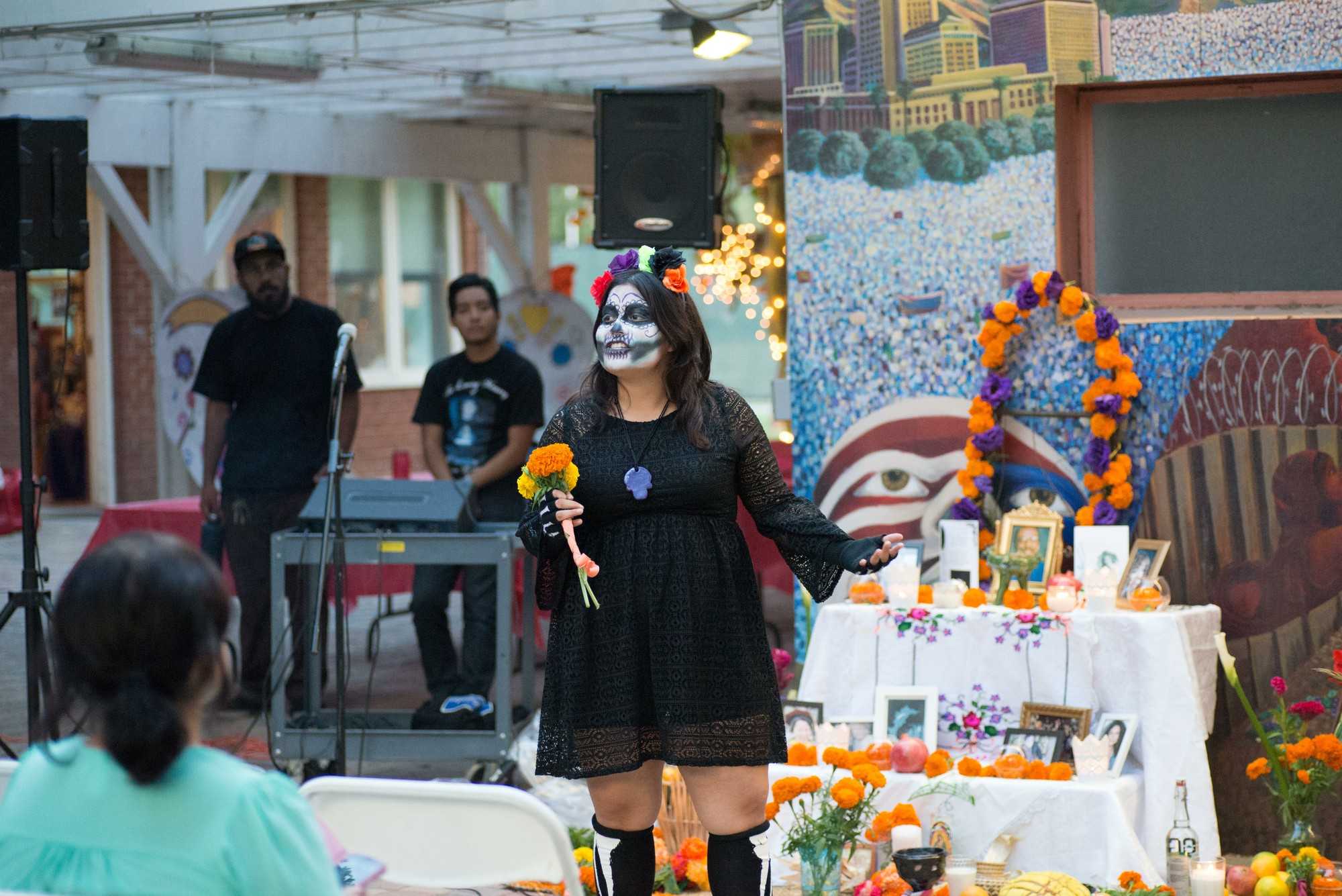 Woman shown in skull makeup in front of a Dia de los muertos altar