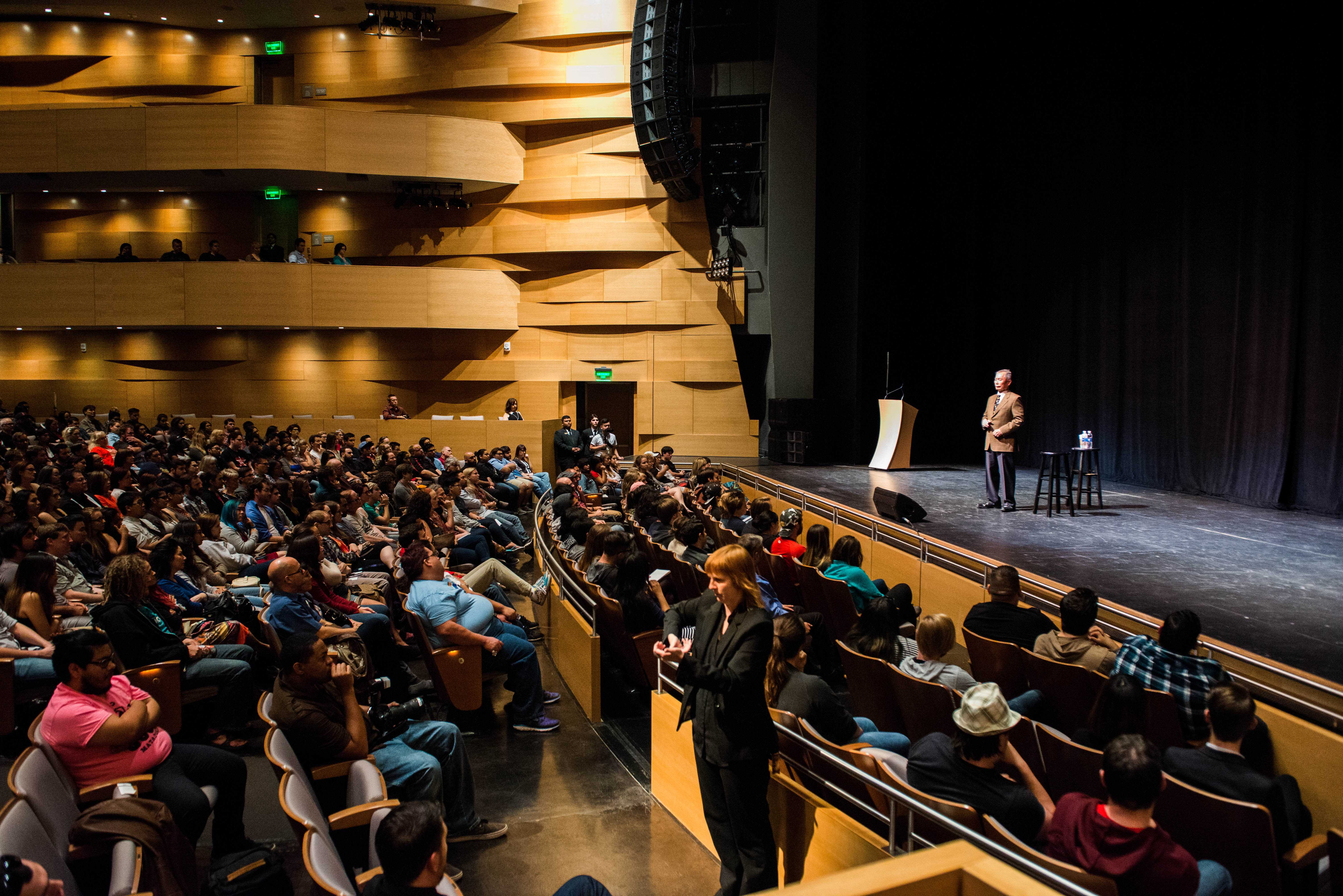 George Takei is shown on the stage with an audience of students