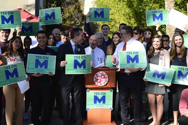 A group of people pose with signs that say, yes on M