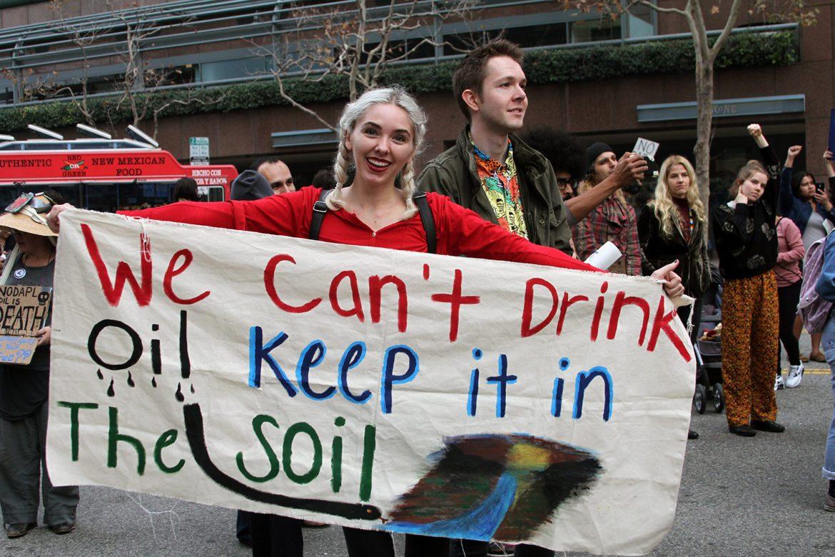 Women holds cloth poster that says, we cant drink oil, keep it in the soil