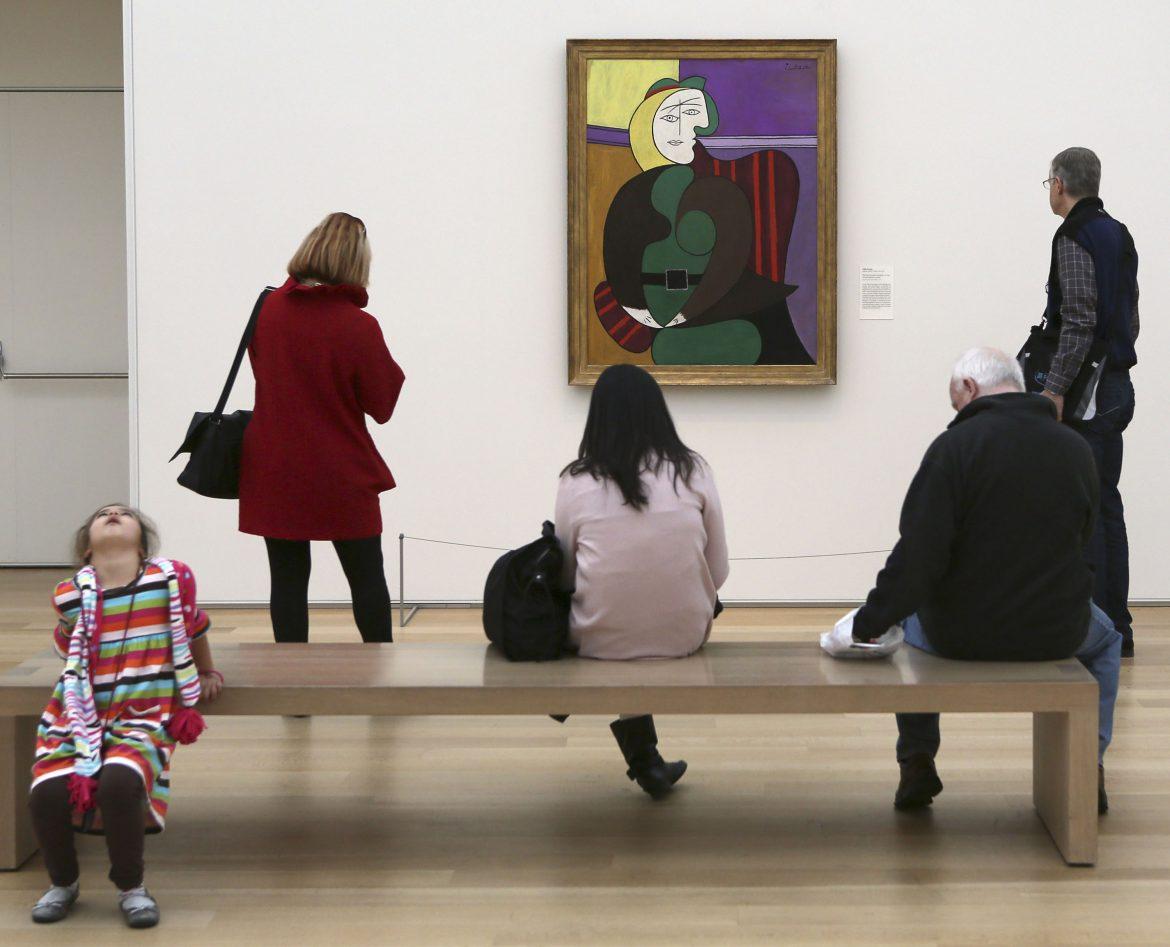 Several people stand in front of picassos red armchair painting which appears to be an abstract image of a woman sitting in a chair