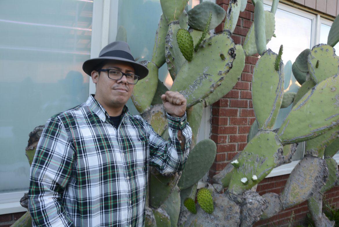 man+pictured+posing+next+to+a+cactus+wearing+a+green+flannel+tshirt+and+a+fedora+hat