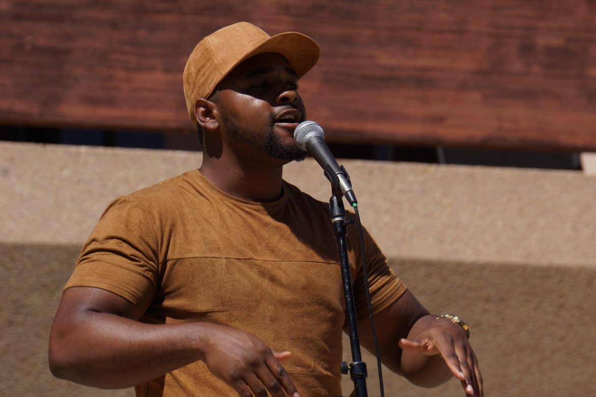 Caleb Word is performing spoken word poetry for Poetry Palooza wearing a matching light brown suede hat and shirt