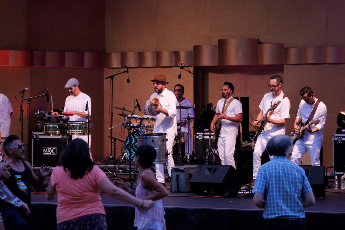 Jungle Fire band members wear matching all white ensembles and concert-goers dance to the music