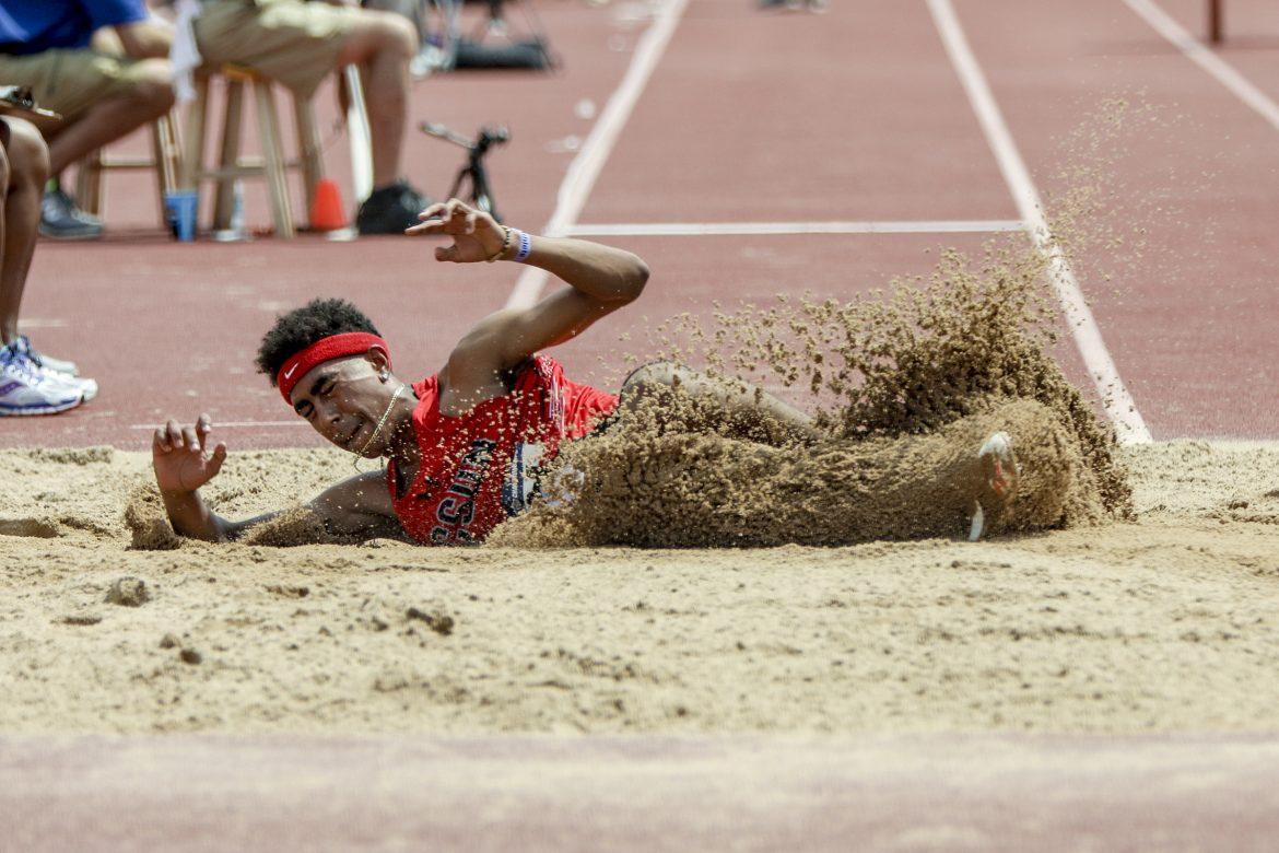 Man pictured sliding through the dirt after completing his long jump