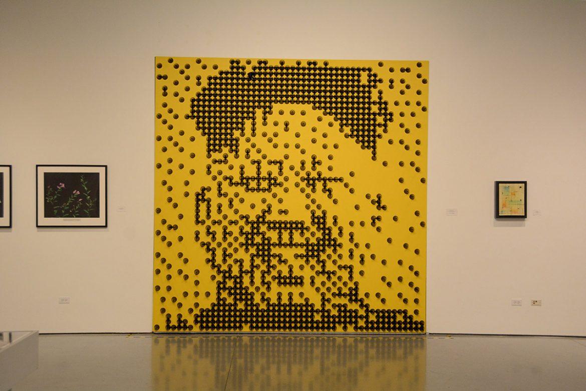 Photo of an art piece in CSUN gallery shows a portrait of Kim Jong Un made on a yellow canvas using brown cones
