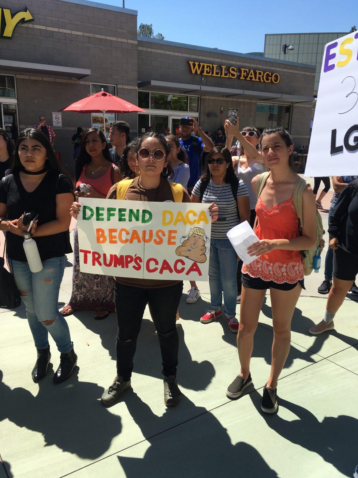 Students protest at csun, one girl holds up a sign that says, defend daca because trumps caca