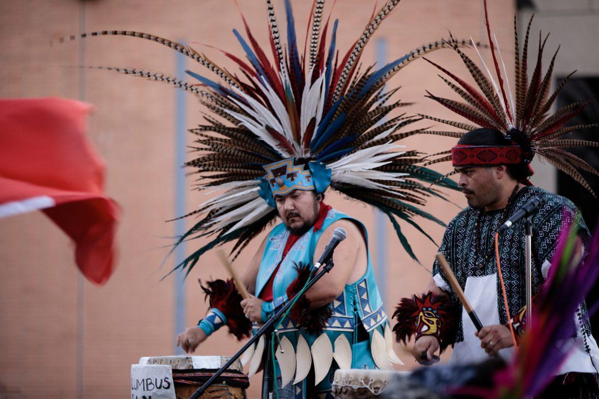 men in blue black and red traditional feathered outfit performing with drums