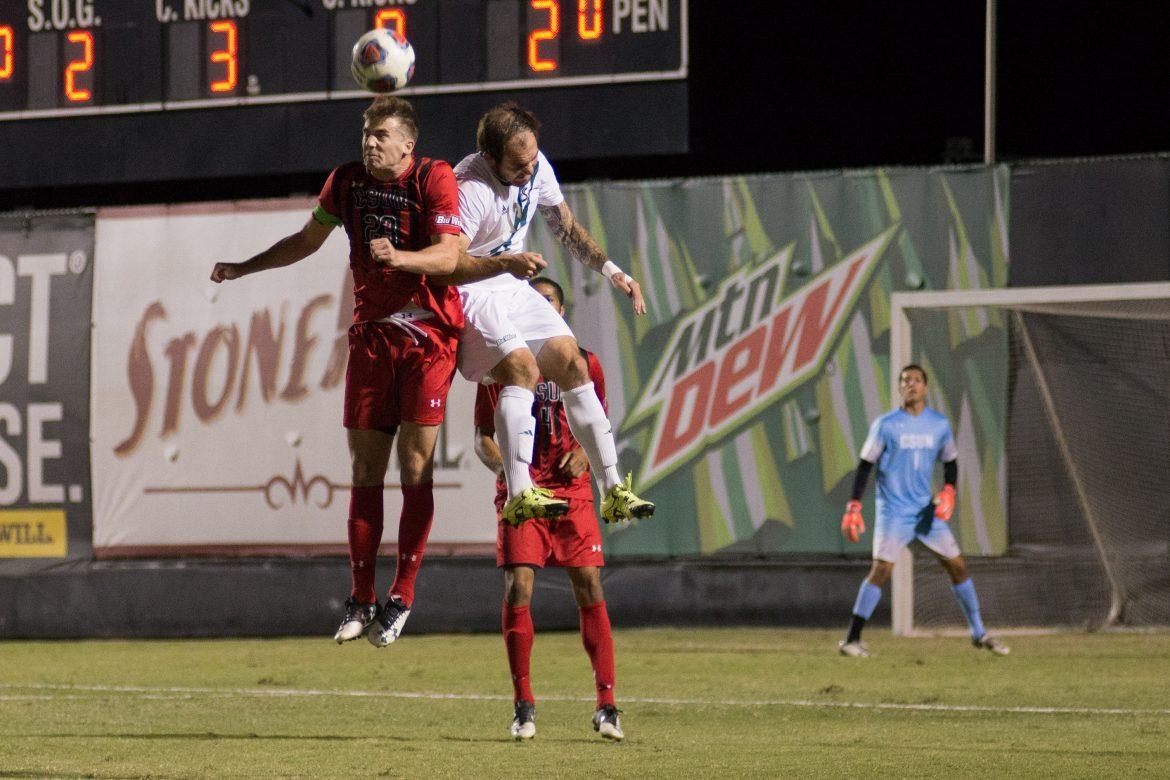 csun+male+soccer+player+in+red+jumping+alongside+player+in+white