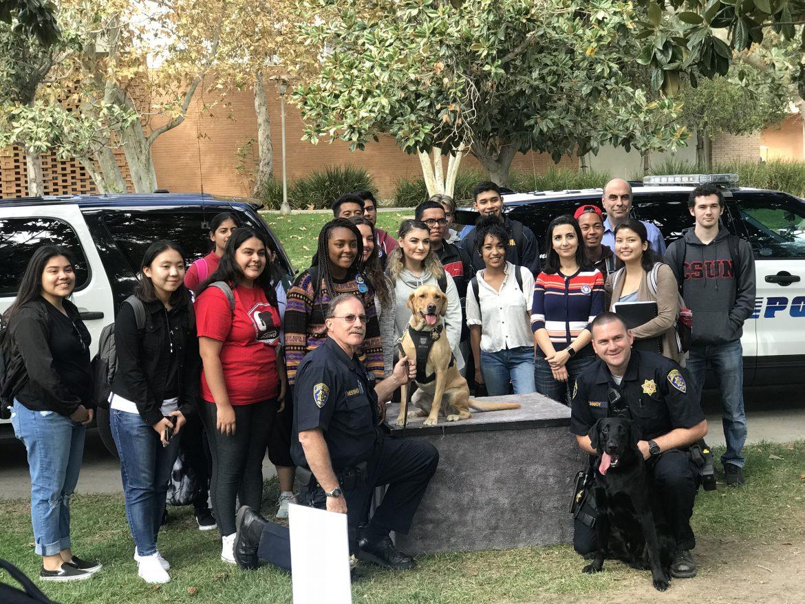 officers dressed in black surrounded by students and brown and lack K9s