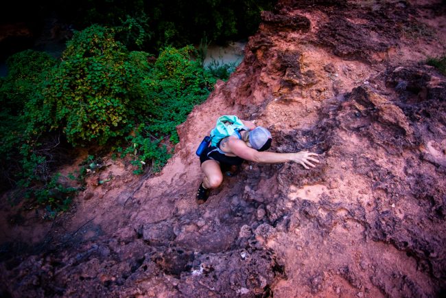 woman with teal back pack climbing rust colored rock