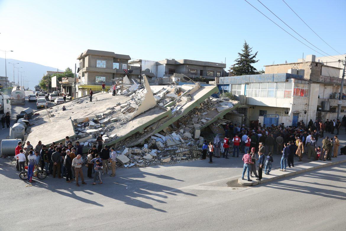 people stand around collapsed building