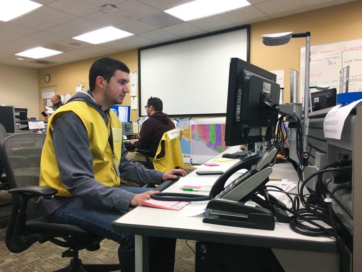 man in yellow vest sits at computer desk