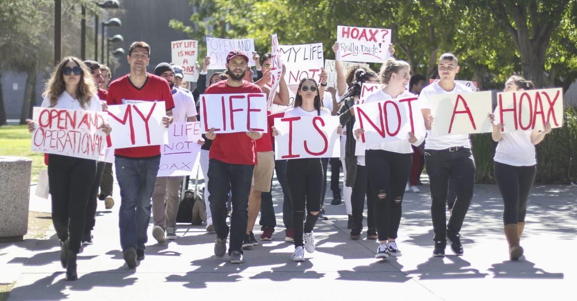 Protesters marching while holding signs reading My Life is Not a Hoax
