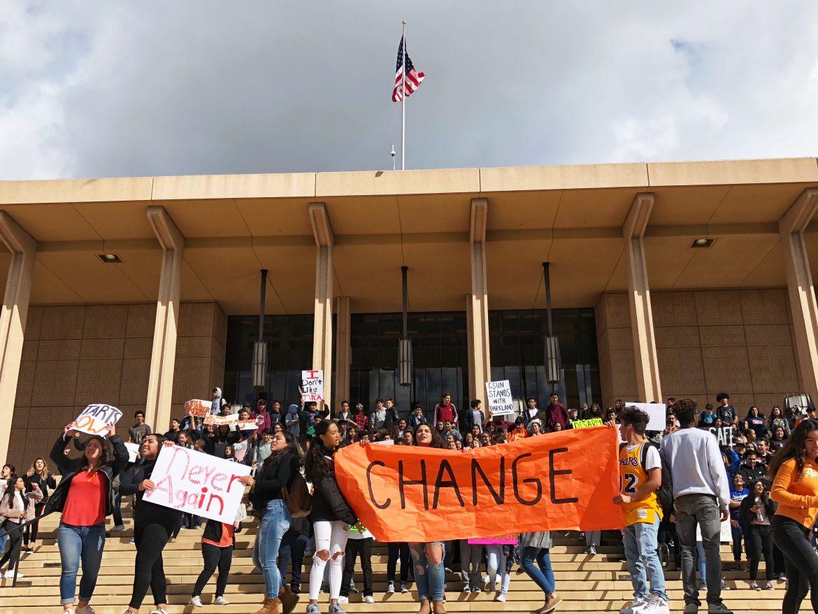students protest in front of the Oviatt Library holding large signs reading change and never again