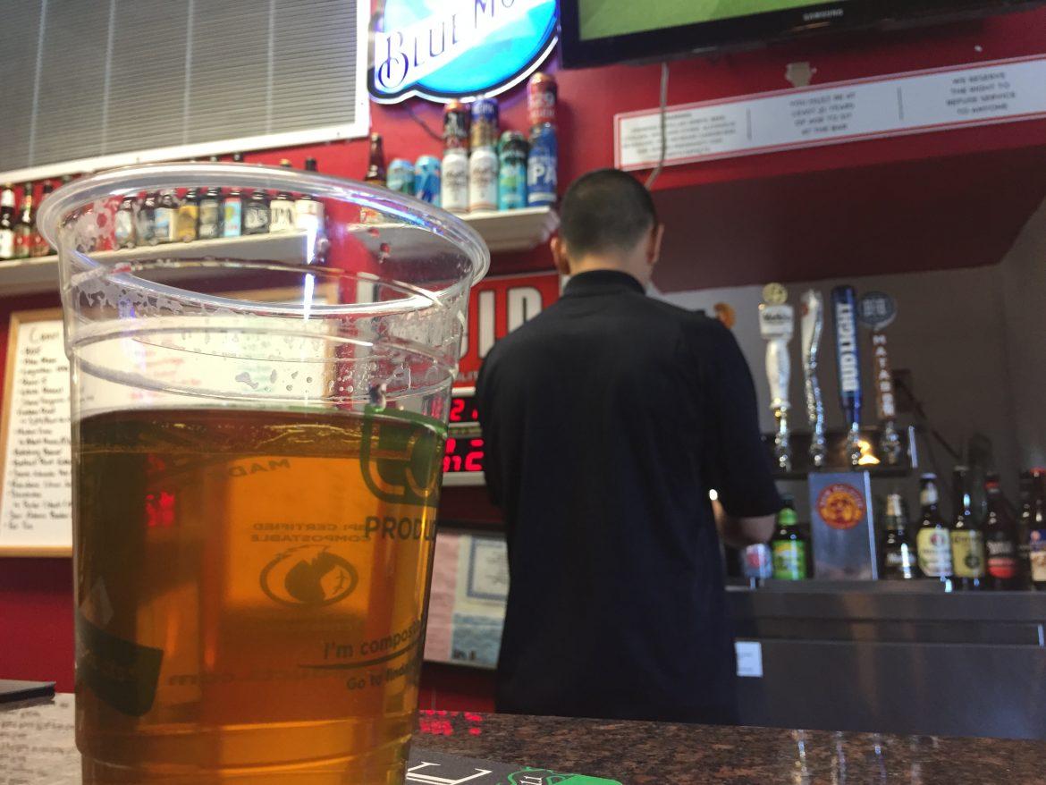 clear cup with beer inside a man with a black shirt with his back turned to the camera