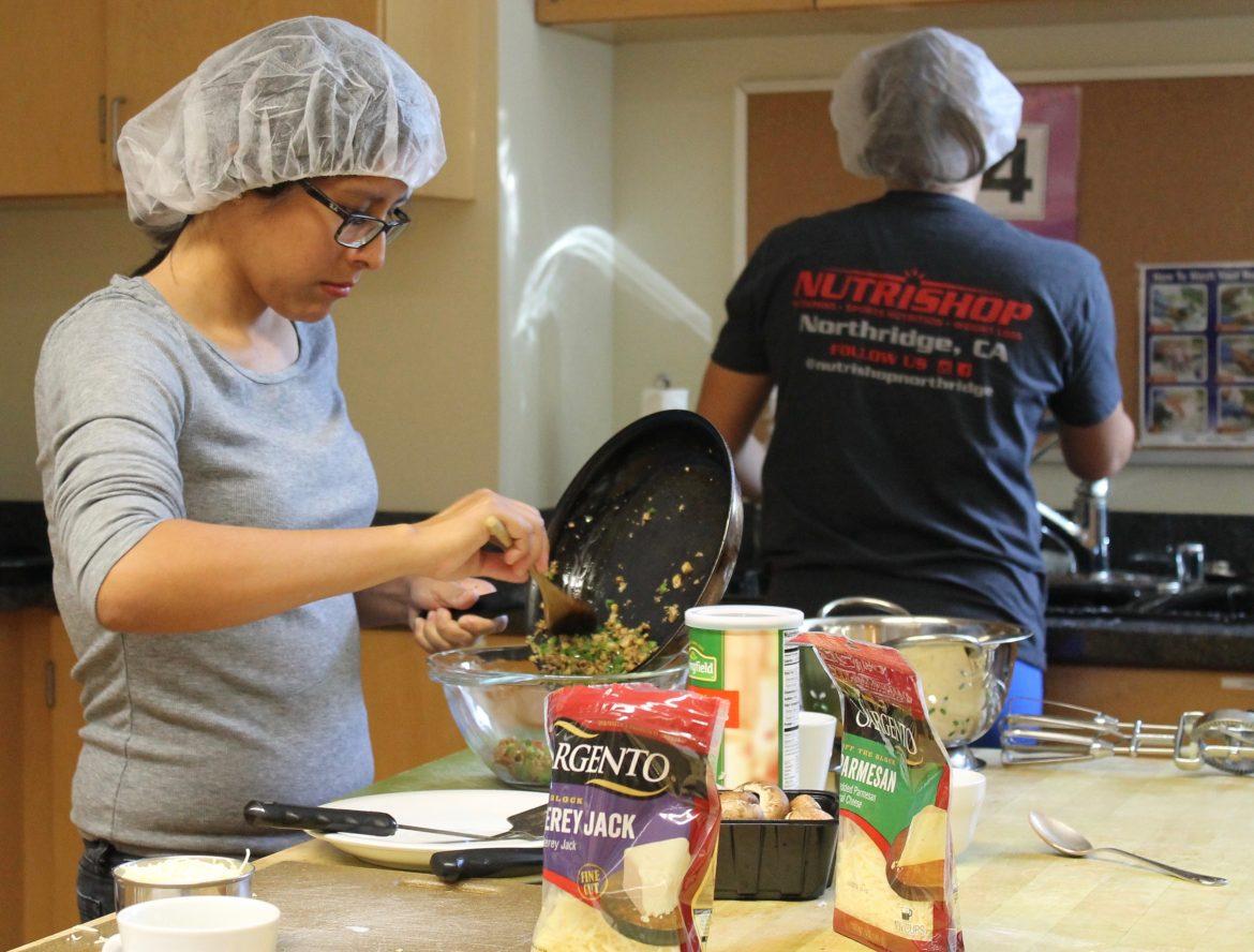 woman in grey shirt and hair net focuses while putting food in a bowl