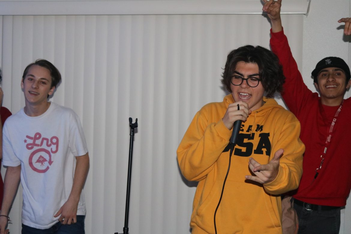 man in yellow sweater holds mic and performs passionately