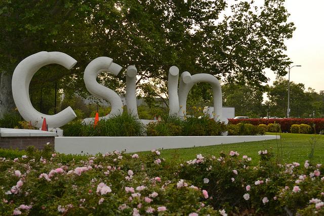 White CSUN letters surrounded by green grass and trees