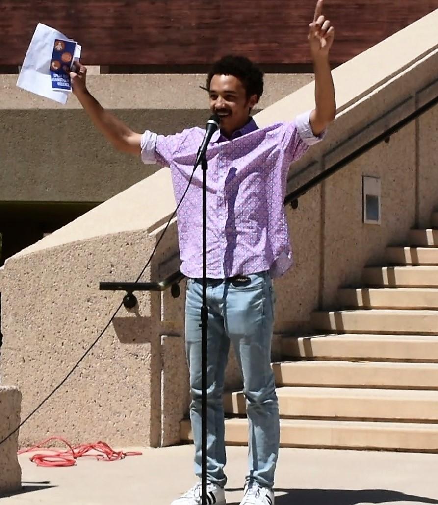 man in purple button down stands with hand in air behind microphone