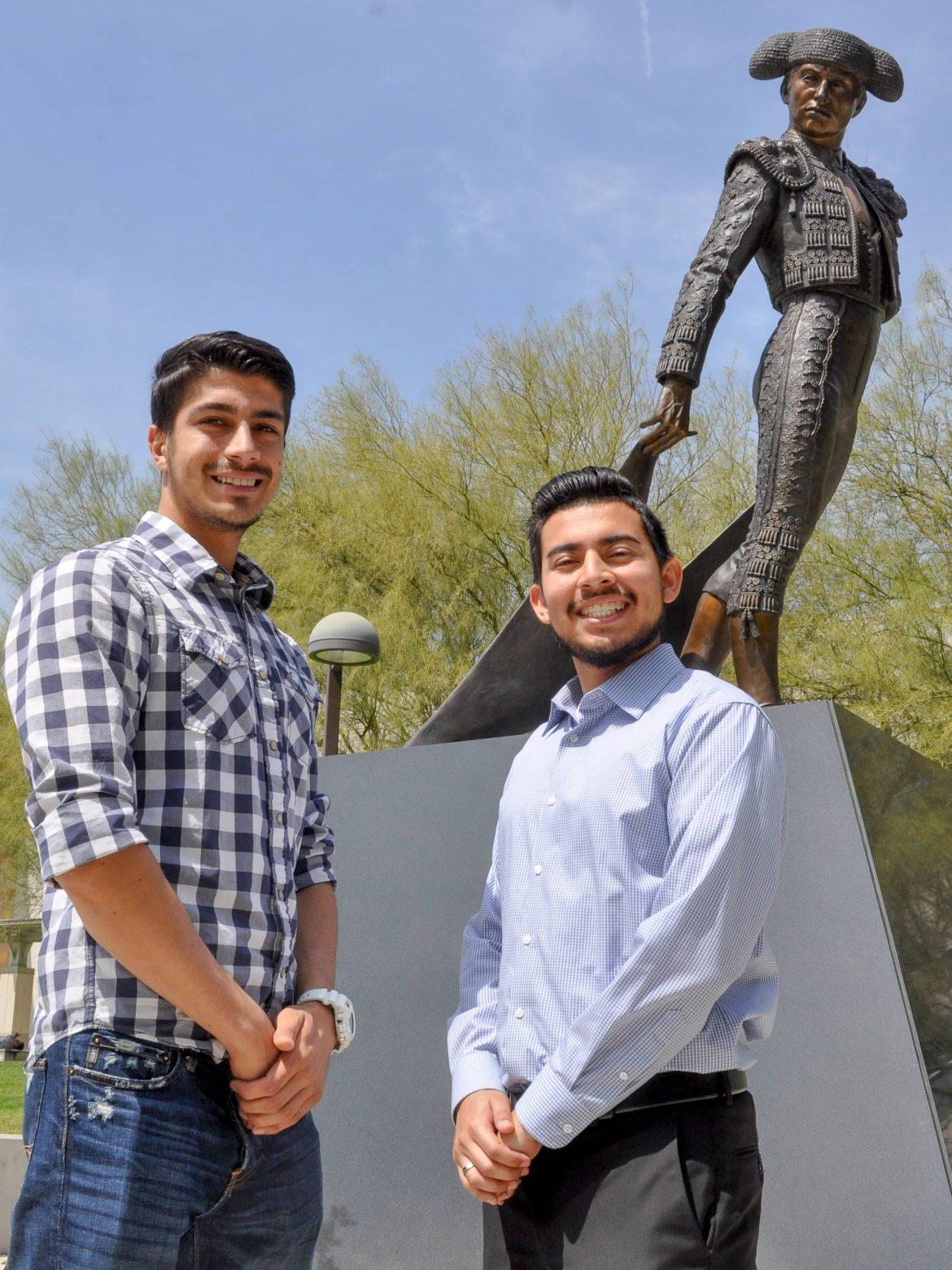 two men happily pose in front the matador statue