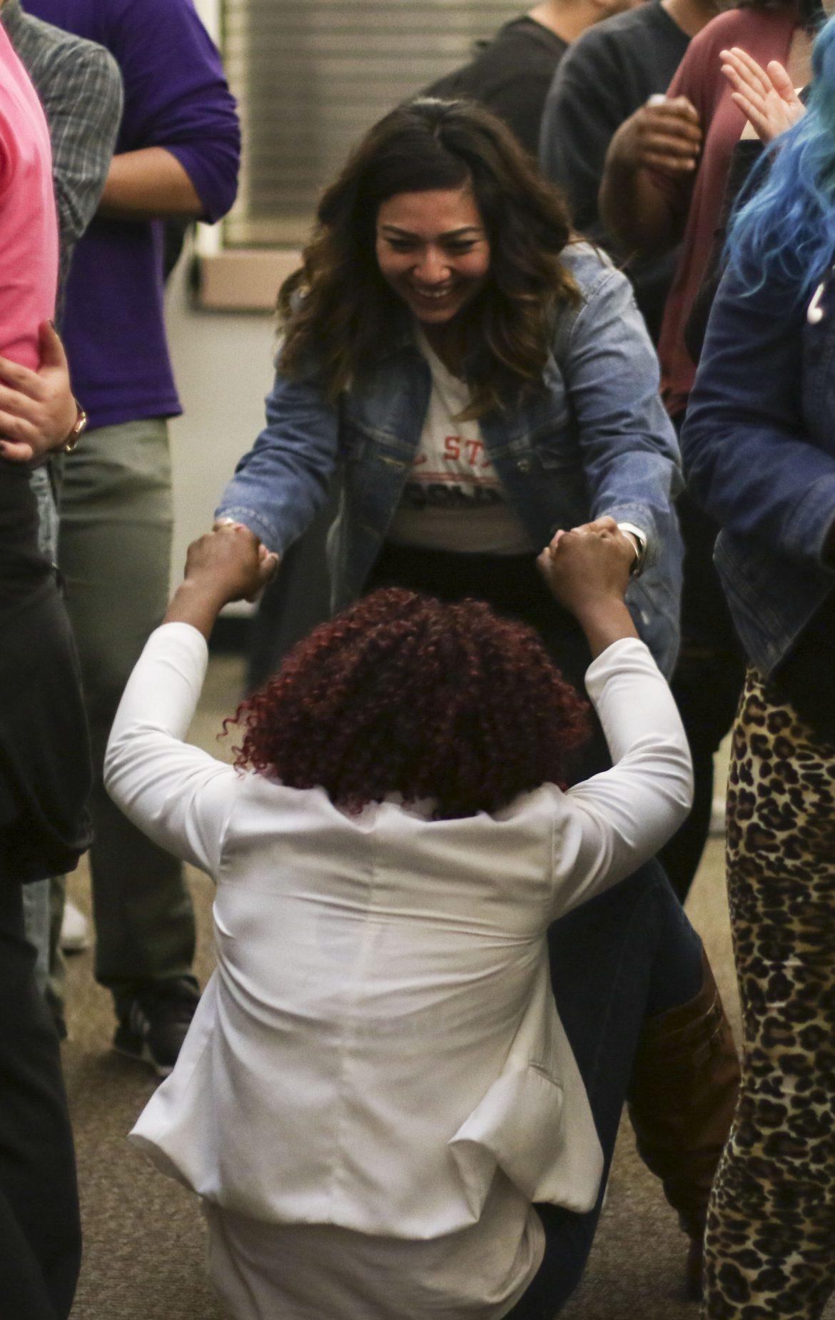 one woman dressed in blue denim jacket happily helps up a woman in white suit