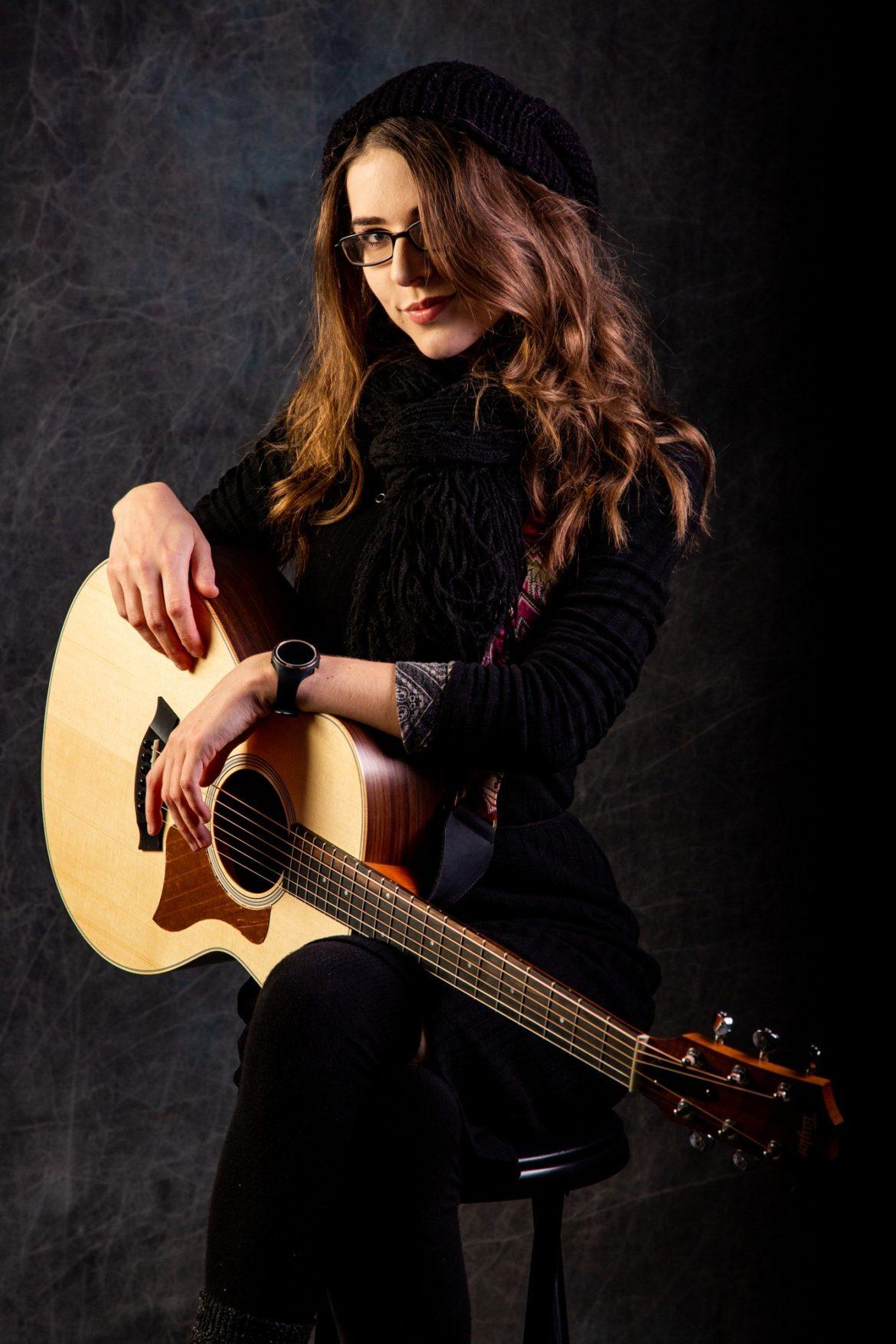 A female musician in a black dress hold a guitar