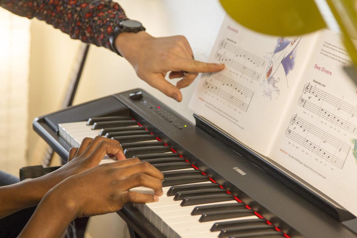 A teacher teacing a student how to play piano by pointing on the playbook.