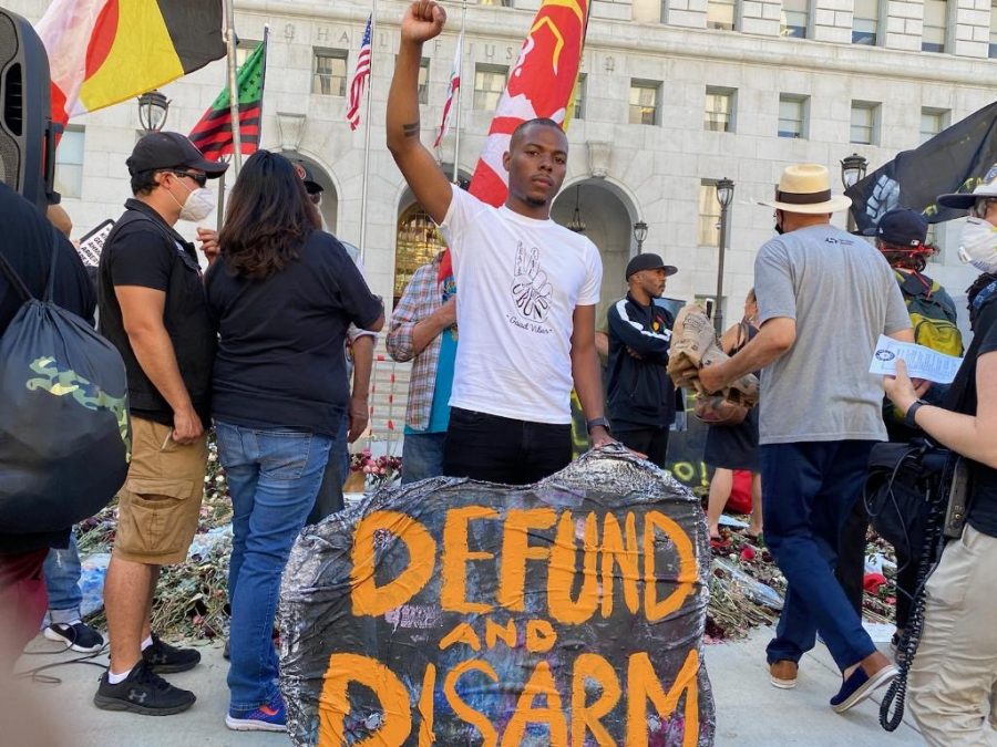 David Cunningham, member and organizer for Black Lives Matter Los Angeles, stands with his fist in the air with a sign that says Defund and disarm.