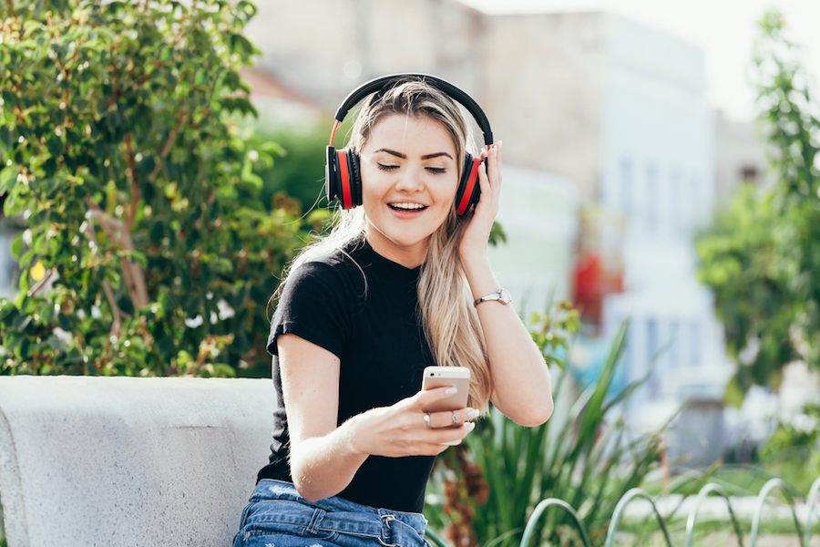 Woman+listening+to+the+music+from+a+smart+phone+with+headphones+in+a+park