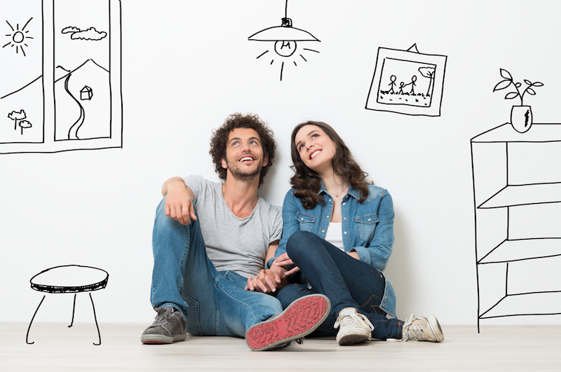 Happy Young Couple Sitting On Floor Looking Up While Dreaming Their New Home