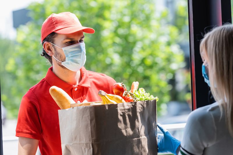man+wearing+a+mask+delivering+to+groceries+to+mask-wearing+woman