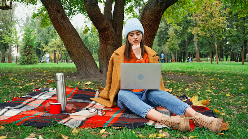 young+woman+sitting+under+a+tree+looking+at+a+laptop