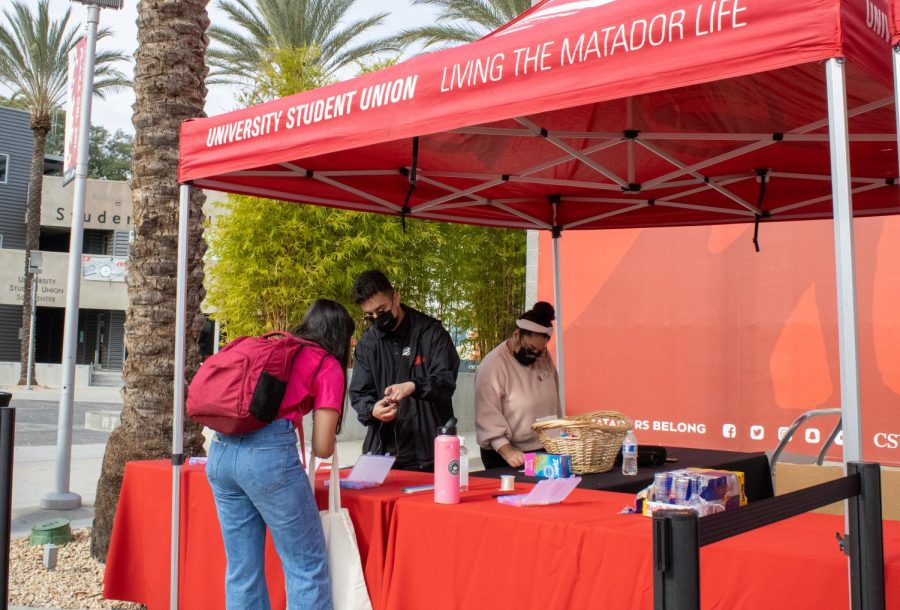 CSUN student taking a ziplock bag of bracelet beads at the USU tent in front of the Northridge Center on Dec. 7,2021. Students are able to take a free red bull and snacks as well.