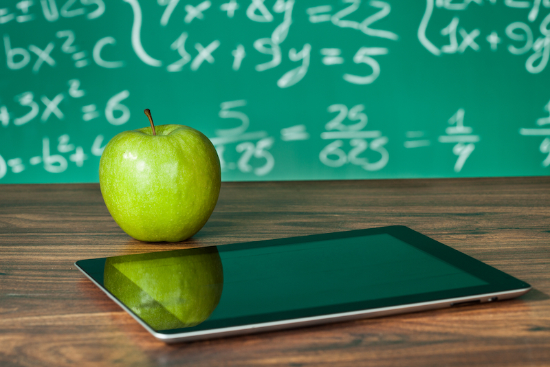 Digital tablet and apple on desk in front of blackboard