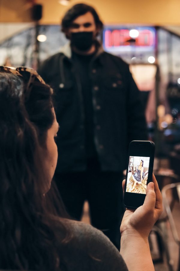 A person holding a phone and facing a picture of a woman and a guy behind the phone, and the person holding it is comparing them