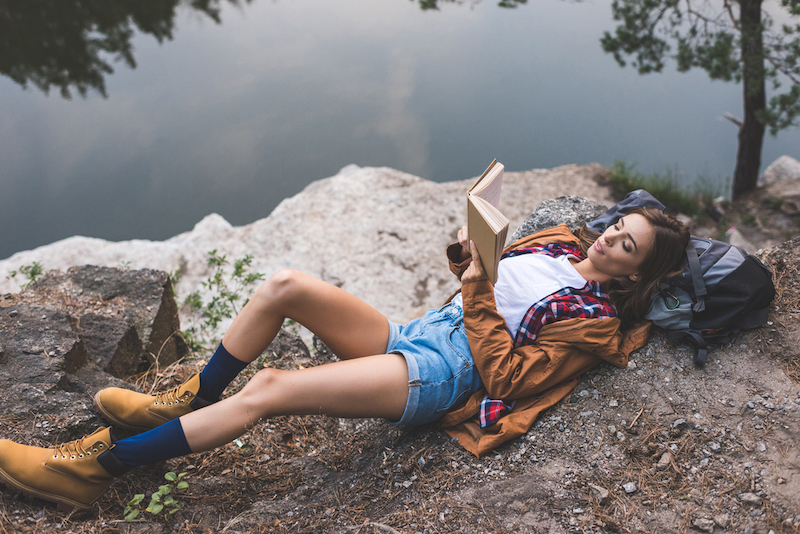 woman+laying+on+a+rock+by+a+lake+and+reading+a+book
