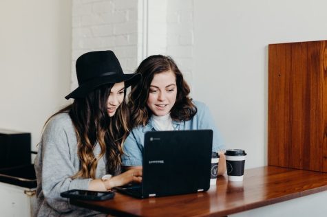 two young women in a cafe looking at a laptop