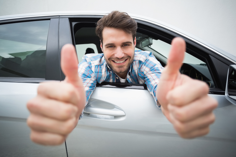 Young man smiling at camera showing thumbs up in his car