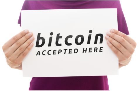 person in a purple shirt holding a sign that says Bitcoin accepted here