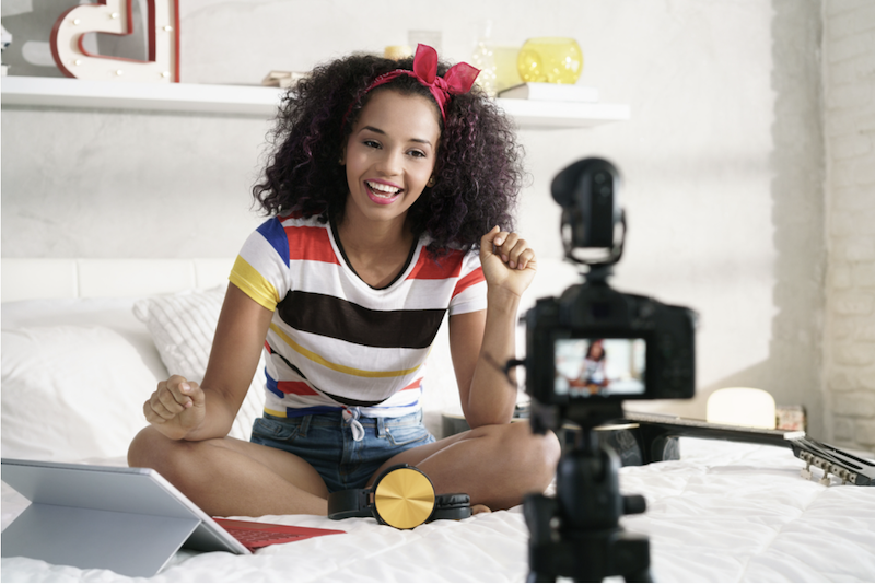 Girl in striped shirt sitting on a bed and talking into a camera