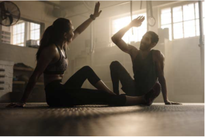 man and woman giving a high five in a gym while sitting on the floor