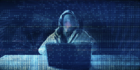 person wearing hoodie and mask sitting in front of computer