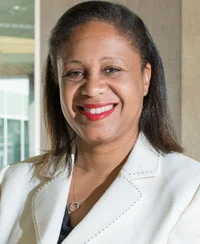 A black woman with brown hair smiling to a picture. She is dressing with a white clothes and red lipstick